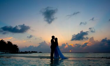 A couple shares a romantic moment on a tropical beach during a beautiful sunset, symbolizing love and serenity.