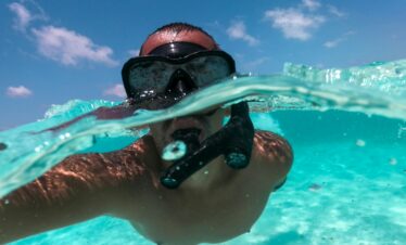 Person snorkeling in clear blue water on a sunny day, capturing an underwater view.