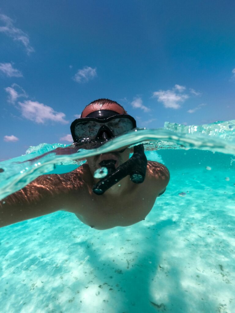 Person snorkeling in clear blue water on a sunny day, capturing an underwater view.