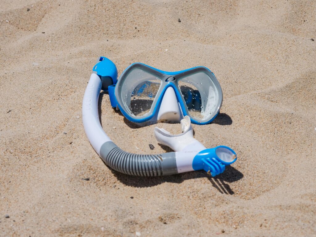 Blue snorkel mask set on a sandy beach, ideal for travel and summer themes.