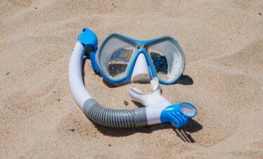 Blue snorkel mask set on a sandy beach, ideal for travel and summer themes.